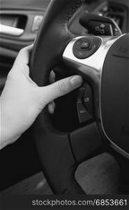 Closeup black and white photo of female driver adjusting cruise control system on steering wheel
