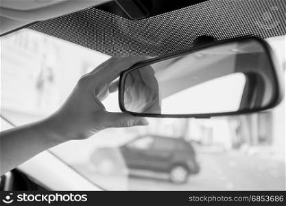 Closeup black and white photo of female driver adjusting rear view mirror