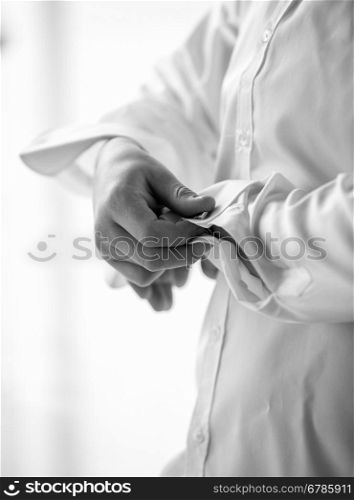 Closeup black and white photo of man adjusting cufflinks on white shirt
