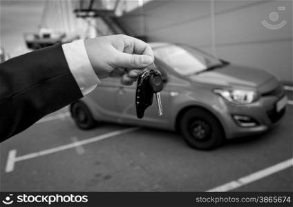 Closeup black and white photo of man in suit holding car keys against new car