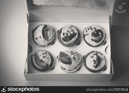 Closeup black and white photo of open box with 6 cupcakes with strawberry