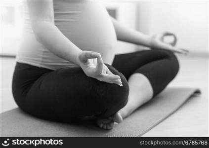 Closeup black and white photo of pregnant woman practicing yoga on floor at home