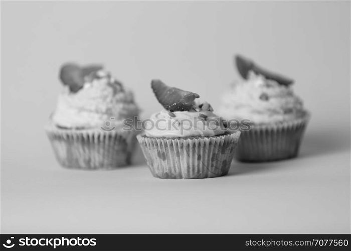 Closeup black and white photo of three tasty cupcakes over background in studio
