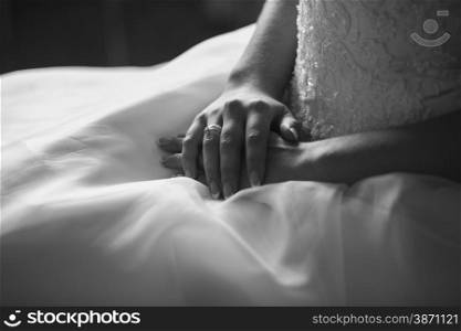Closeup black and white shot of bride holding hands on wedding dress