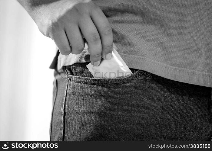 Closeup black and white shot of man putting condom in jeans pocket