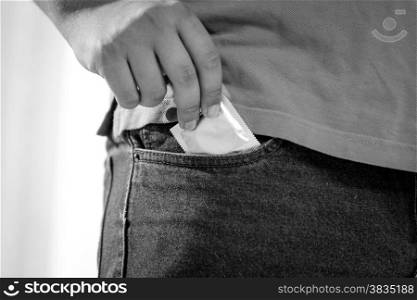 Closeup black and white shot of man putting condom in jeans pocket