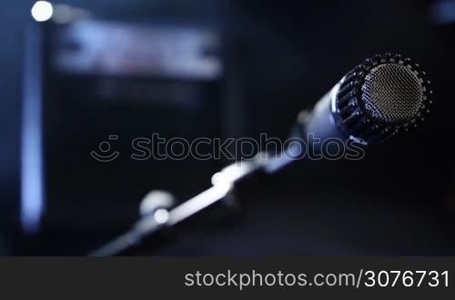 Closeup black microphone plugging in with audio cord to record guitar sound in studio over blurred guitar amplifier background.