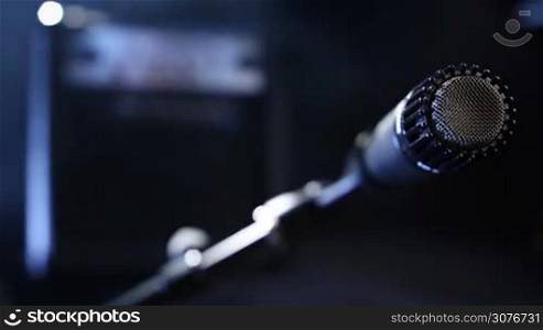 Closeup black microphone plugging in with audio cord to record guitar sound in studio over blurred guitar amplifier background.