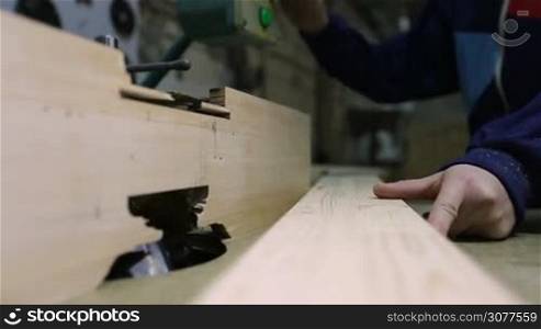Closeup carpenter&acute;s hands cutting wooden plank on table saw with sawdust flying. Skilled craftsman working with circular saw and cutting board in workshop.