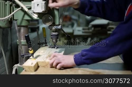Closeup carpenter&acute;s hands drilling holes in wooden board using vertical drilling machine in workshop. Drilling holes in wooden board with saw dust flying in carpentry woodwork shop.