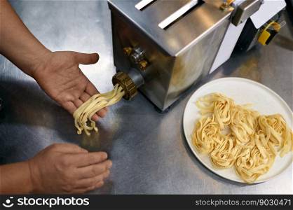 Closeup chef using pasta maker on restaurant kitchen. Handmade noodles preparation recipe. Focus on cooker hand holding freshly made spaghetti. Closeup chef using pasta maker on restaurant kitchen