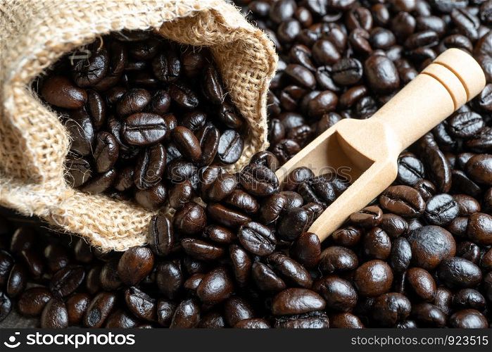 Closeup Coffee beans in bag made from burlap on wooden surface and wooden shovel lying in a sack. Fresh coffee beans and bag on old wood.