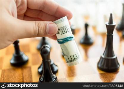 Closeup conceptual photo of man making move at chess game with dollar bills