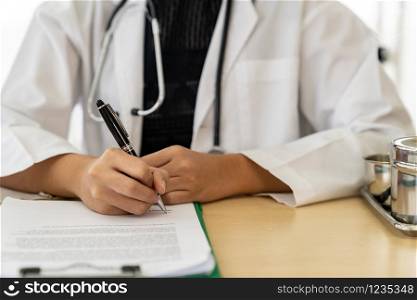 Closeup confident female doctor medical professional sitting in examination room in hospital clinic sign document. No face crop