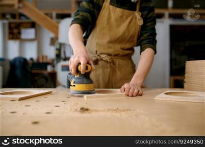 Closeup craftsman hands working with eccentric grinding machine at carpentry workshop. Orbital sanding process. Closeup craftsman hands working with eccentric grinding machine