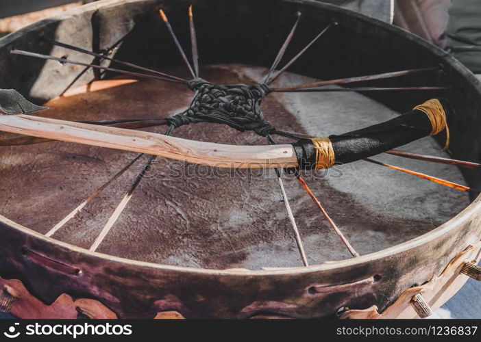 Closeup detail of a shamanic spiritual meditation ritual leather drum with a natural handmade wild wood branch drumstick for a primitive shamanism ceremony- Concept of mystical paganism or alternative lifestyle boho gypsy culture.