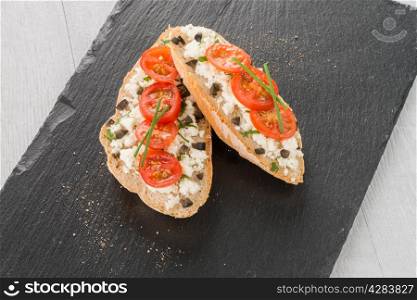 Closeup detail of bread with cottage and tomato over black ardoise tray.