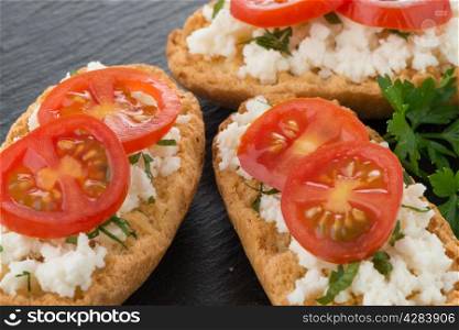 Closeup detail of bread with cottage and tomato over black ardoise tray.