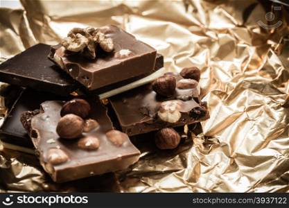 Closeup different sorts chocolate pieces and hazelnuts. Variety of chocolates on golden foil wrapping.