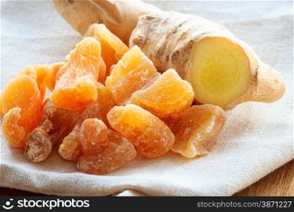 Closeup dried candied crystallized ginger pieces and fresh rhizome root on rustic table. Healthy eating, home remedy for nausea, colds.