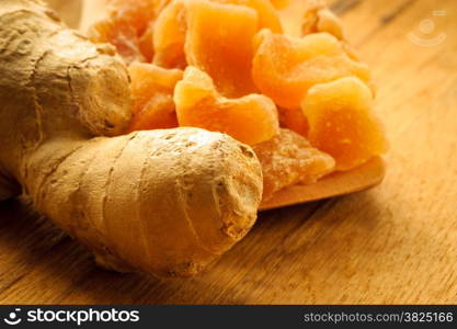 Closeup dried candied crystallized ginger pieces and fresh root on wooden table. Healthy food, home remedy for nausea, colds.