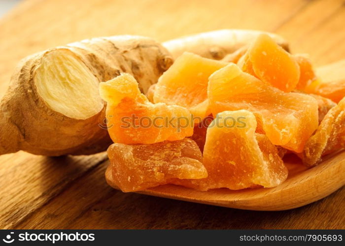 Closeup dried candied crystallized ginger pieces and fresh root on wooden table. Healthy food, home remedy for nausea, colds.