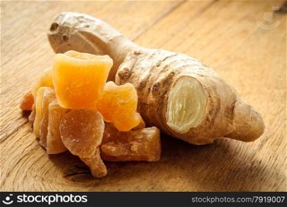 Closeup dried candied crystallized ginger pieces and fresh root on wooden table. Healthy food, home remedy for nausea, colds.