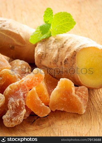 Closeup dried candied crystallized ginger pieces and raw root on wooden table. Healthy food, home remedy for nausea, colds.