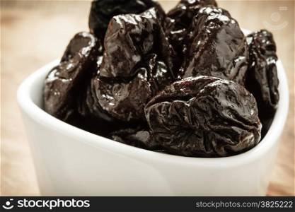 Closeup dried plums prunes fruits in white bowl on wooden rustic table background