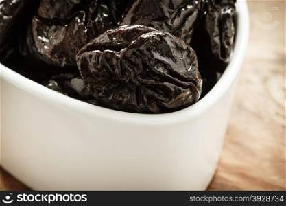 Closeup dried plums prunes fruits in white bowl on wooden rustic table background