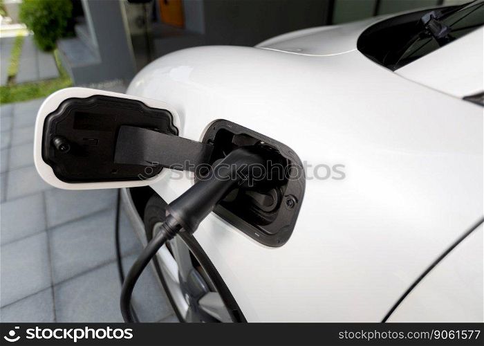 Closeup electric vehicle plugged-in with cable from charging point powered for progressive concept by alternative clean energy rechargeable EV car at home charging station.. EV car plugged-in with cable from progressive home charging station.