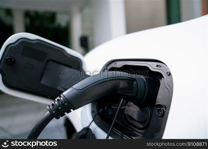 Closeup electric vehicle plugged-in with cable from charging point powered for progressive concept by alternative clean energy rechargeable EV car at home charging station.. EV car plugged-in with cable from progressive home charging station.