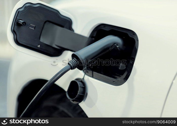 Closeup electric vehicle plugged-in with cable from charging station powered for progressive environmental automotive industry concept by alternative clean energy rechargeable EV car at charging point. EV car plugged-in with cable from charging station for progressive concept