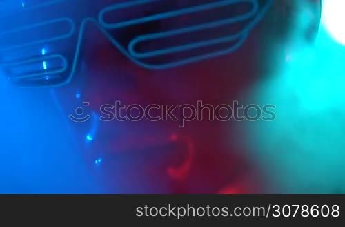 Closeup face of female mannequin in blue glowing led glasses over dark smokey background