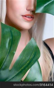 Closeup facial portrait personable woman with perfect smooth makeup holding green monstera leaves and cover her face as natural healthy skincare treatment. Tropical nature and beauty concept. Closeup facial portrait personable woman holding green monstera.