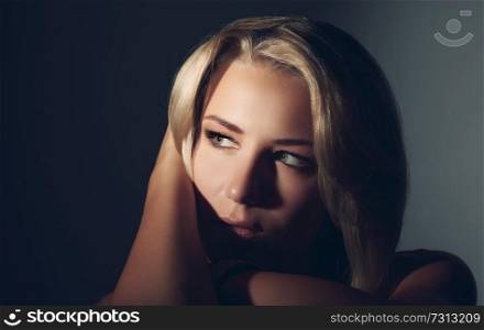 Closeup fashion portrait of a beautiful blond woman over dark background, sensual female with seductive look
