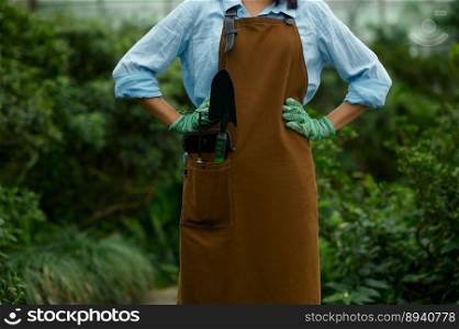 Closeup female gardener in overalls with garden small shovel and rake tool in pocket. Gardening and farming hobby concept. Closeup female gardener in overalls with garden tool in pocket