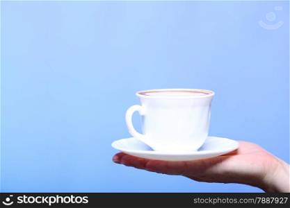Closeup female hand holding a cup of latte coffee cappuccino hot drink in autumn winter time copyspace blue background