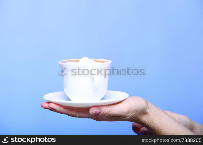 Closeup female hand holding a cup of latte coffee cappuccino hot drink in autumn winter time copyspace blue background