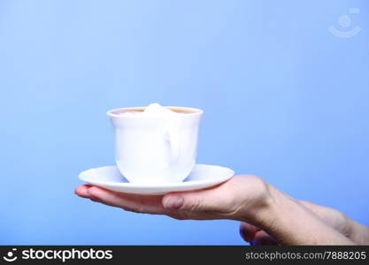 Closeup female hand holding a cup of latte coffee cappuccino hot drink in autumn winter time copyspace blue background