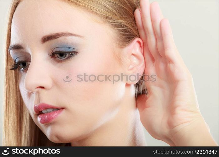 Closeup female hand to ear listening on gray. Gossip girl with palm behind ear spying. Young woman listening secret.