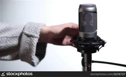 Closeup female hands adjusting pop filter on microphone in sound studio on white background. Vocal recording setup containing a professional microphone and pop filter.