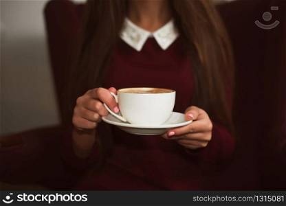 Closeup female hands holding a cup of coffee on saucer.