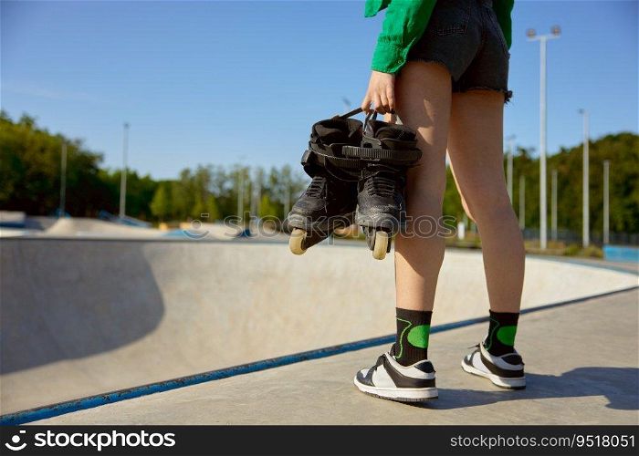 Closeup female teenager with rollers standing front of skating ramp. Preparation for sports training with professional equipment. Closeup female teenager with rollers standing front of skating ramp