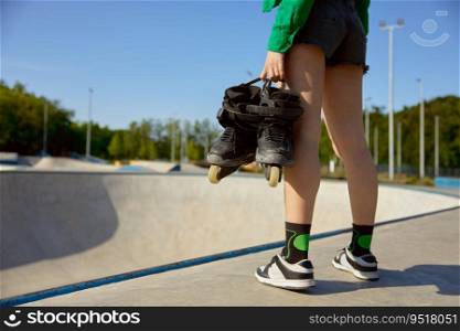 Closeup female teenager with rollers standing front of skating ramp. Preparation for sports training with professional equipment. Closeup female teenager with rollers standing front of skating ramp