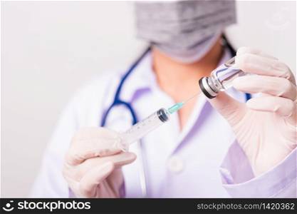 Closeup female woman doctor, nurse or scientist in uniform wearing face mask protective in lab use holding and syringe injecting to vial vaccine bottle, medical outbreak coronavirus COVID-19 concept