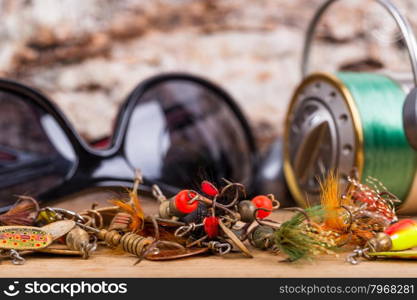 closeup fishing bait lures and reel with line on wooden background