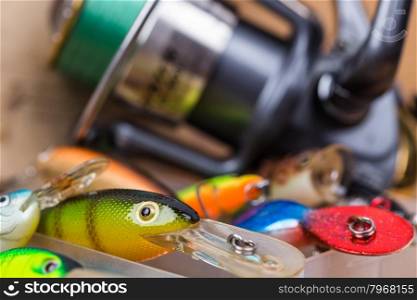 closeup fishing baits wobbler in box with reel and cap on wooden background with selective focus