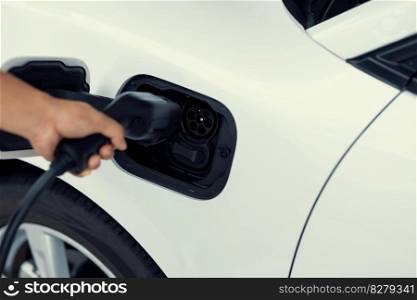 Closeup focus hand insert EV charger plug to electric vehicle from charging station. Progressive alternative clean energy engine car technology. Renewable EV car for eco-friendly transportation idea.. Closeup focus hand insert EV charger to progressive electric rechargeable car.