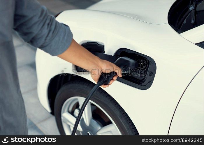 Closeup focus hand insert EV charger plug to electric vehicle from charging station. Progressive alternative clean energy engine car technology. Renewable EV car for eco-friendly transportation idea.. Closeup focus hand insert EV charger to progressive electric rechargeable car.